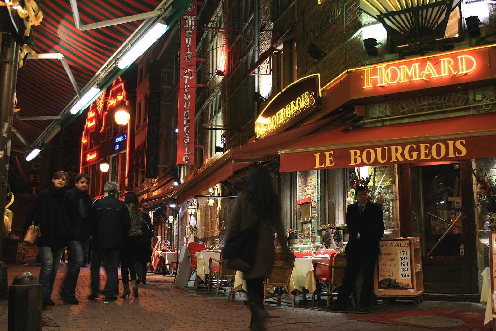 Des enseignes lumineuses de restaurants, parallèles et en drapeau, rue des Bouchers à Bruxelles